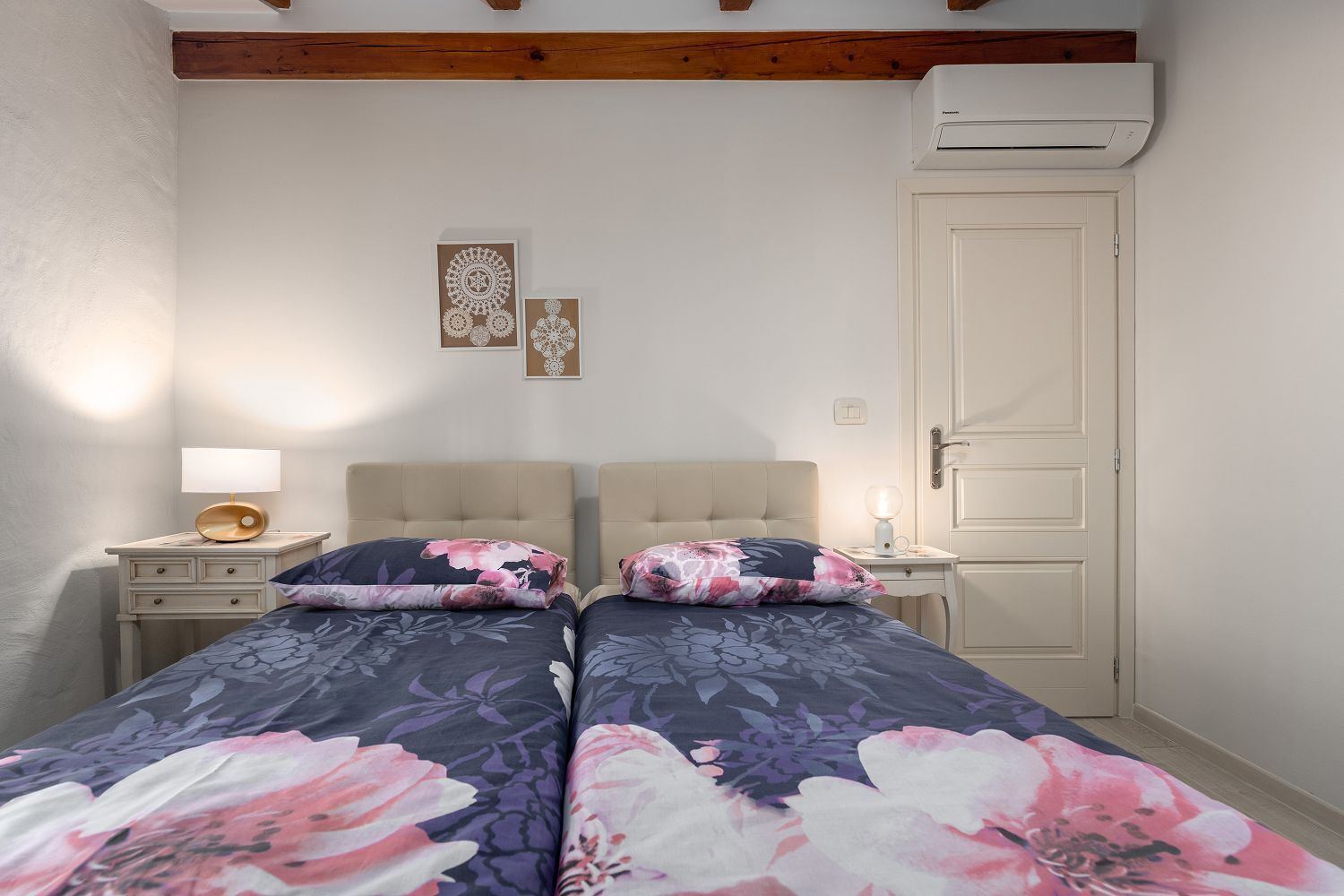 Une chambre avec deux lits, une table de chevet avec une lampe, un climatiseur fixé au mur et une porte.
