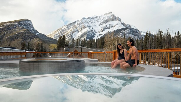 A couple sitting by a hot tub with a mountainous backdrop. - Otter Hotel (Banff)