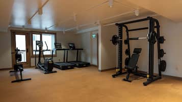 Et rummeligt fitnessrum med løbebånd, crosstrainere og et squat-rack.