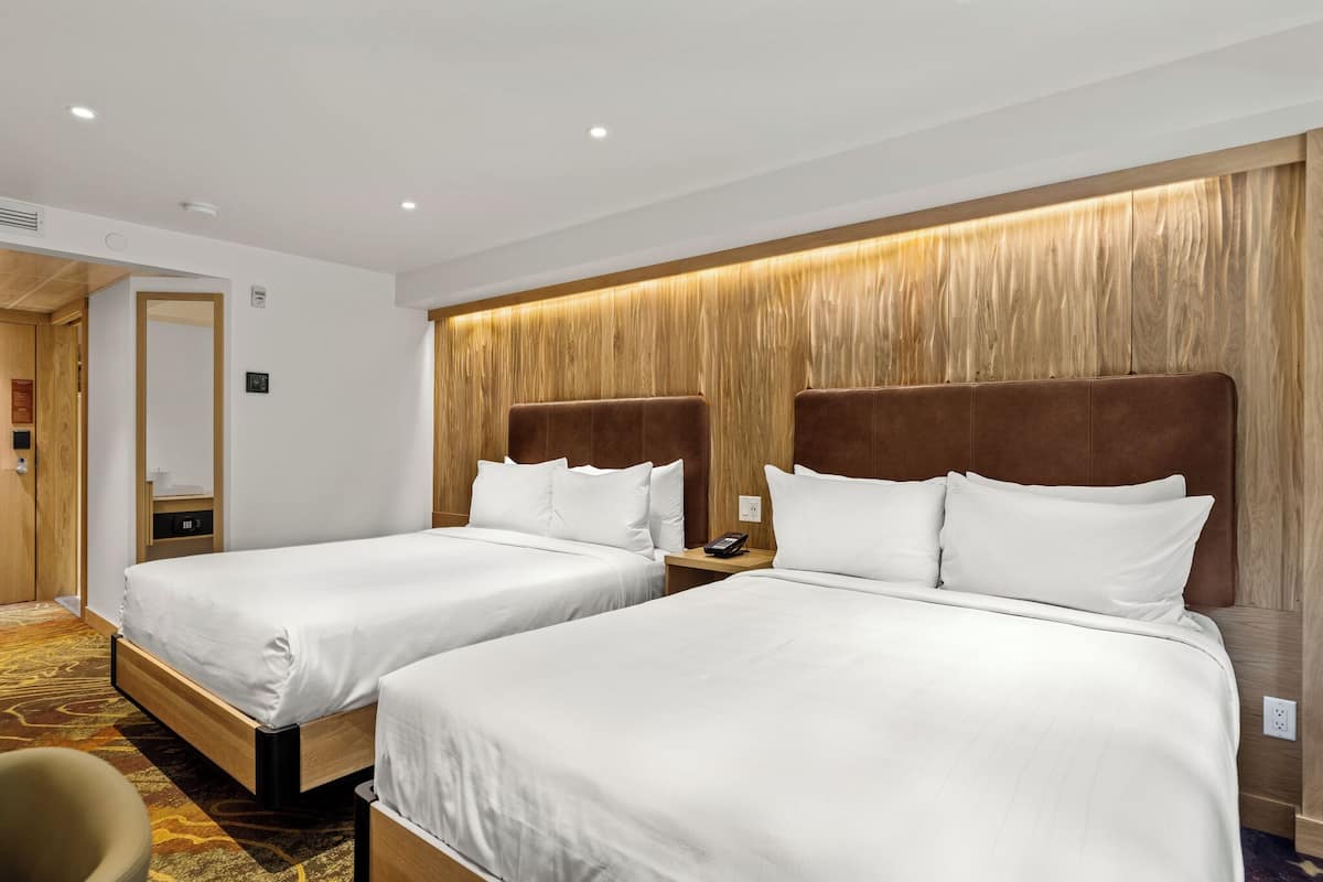 A hotel room with two beds, wooden headboards, and a carpeted floor.