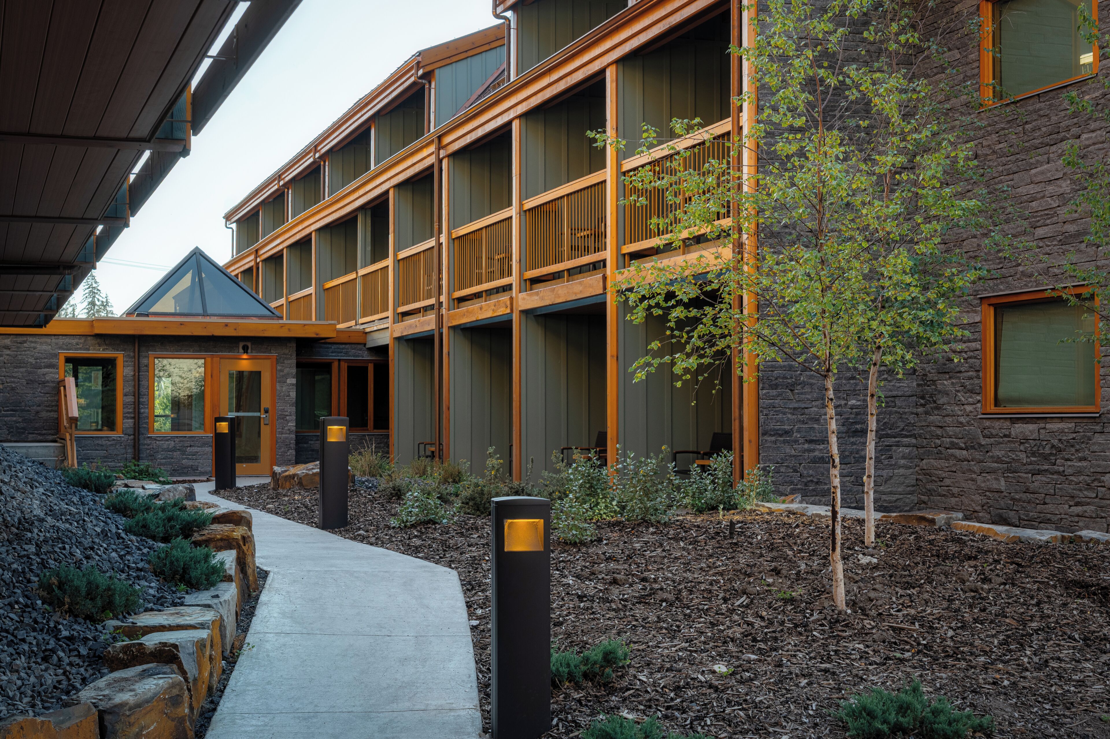 A multi-story building with a stone facade, wooden balconies, and a clear pathway leading to the entrance.