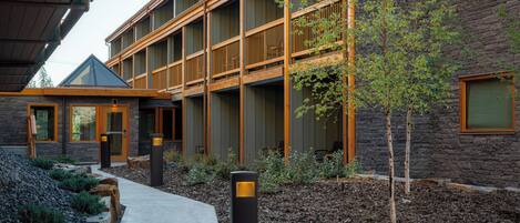 A multi-story building with a stone facade, wooden balconies, and a clear pathway leading to the entrance.