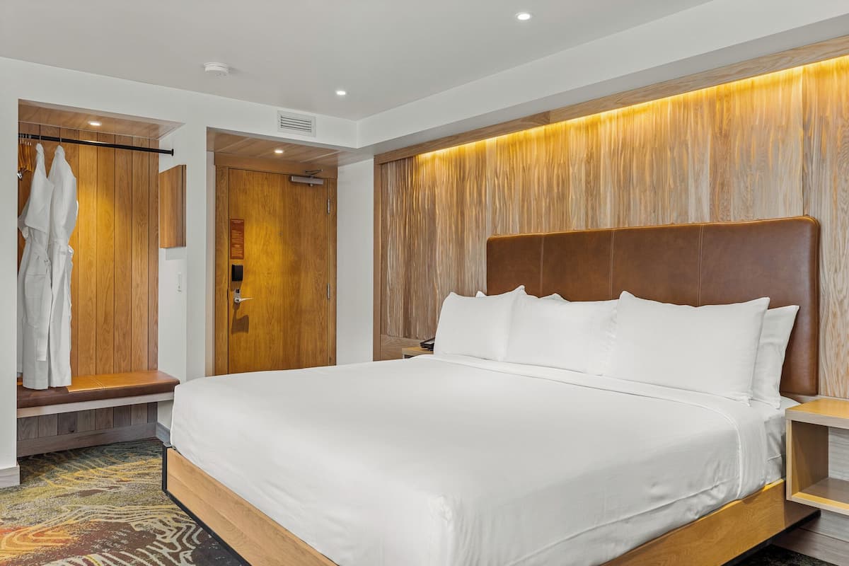 A modern hotel room with a large bed, wooden paneling, and a bench with robes.
