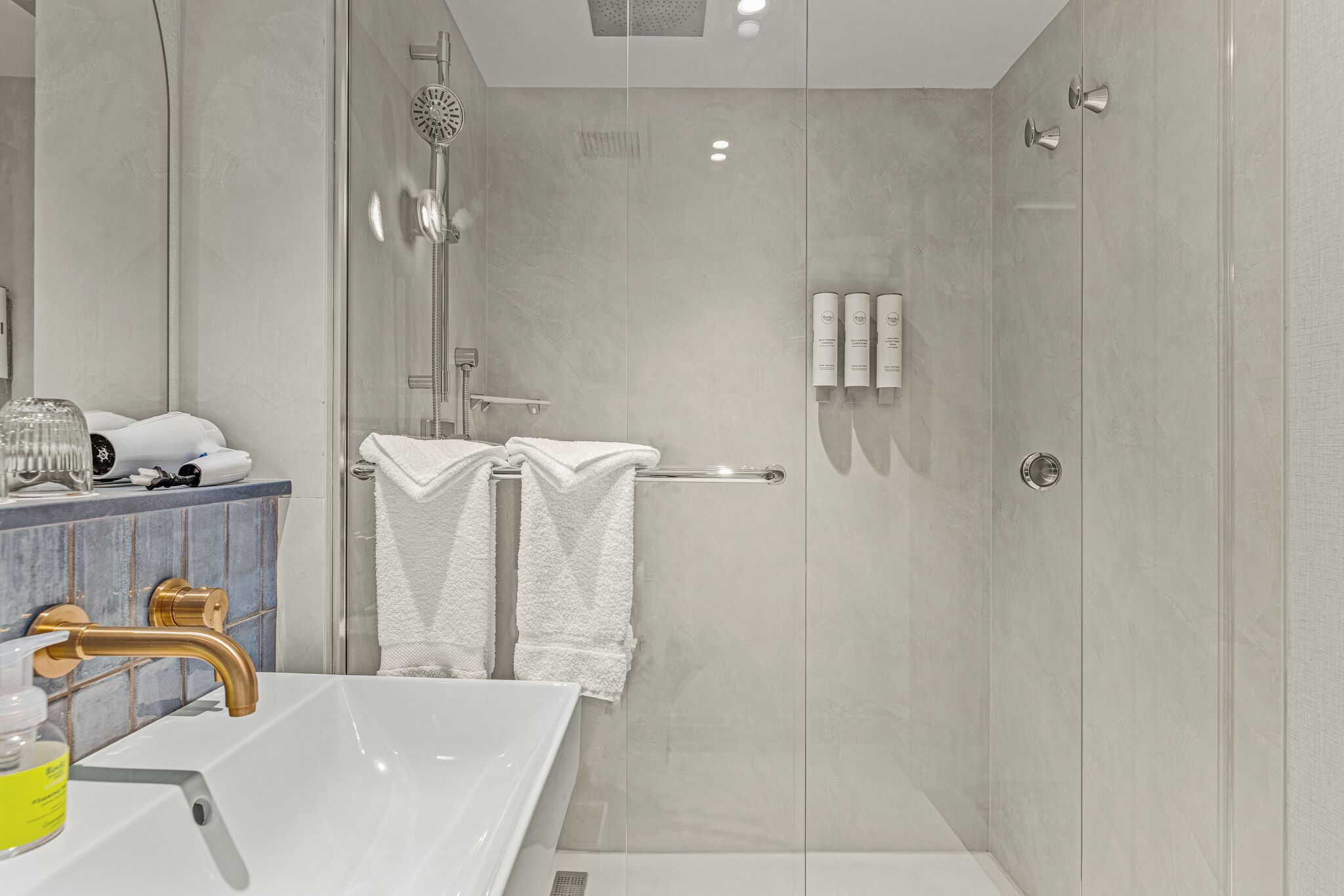 A modern bathroom with a glass-enclosed shower, a white sink with a gold faucet, and a vanity with toiletries.