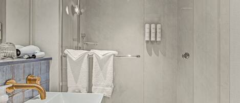 A modern bathroom with a glass-enclosed shower, a white sink with a gold faucet, and a vanity with toiletries.