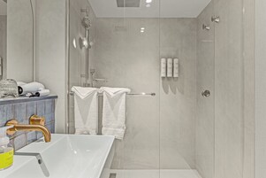 Une salle de bain moderne avec une douche à parois de verre, un lavabo blanc avec un robinet doré et un meuble avec des articles de toilette.