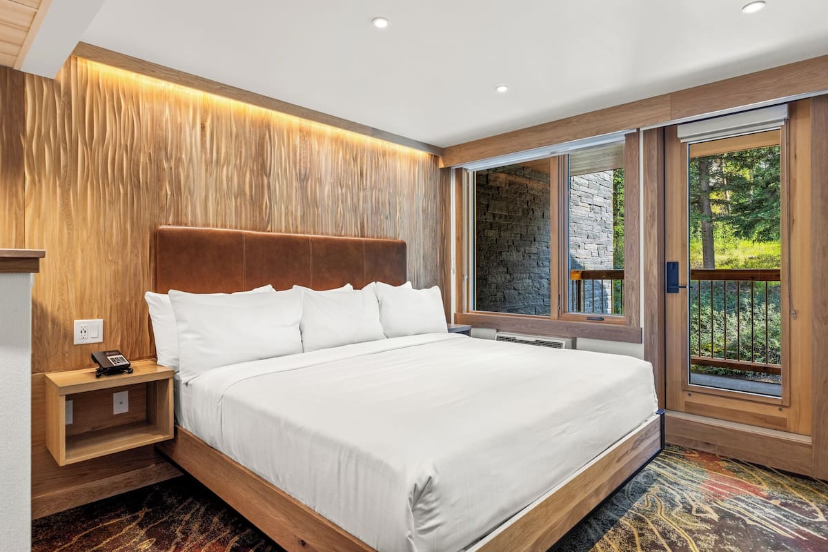 A modern bedroom with a large bed, wooden headboard, and a built-in window offering a view of greenery.