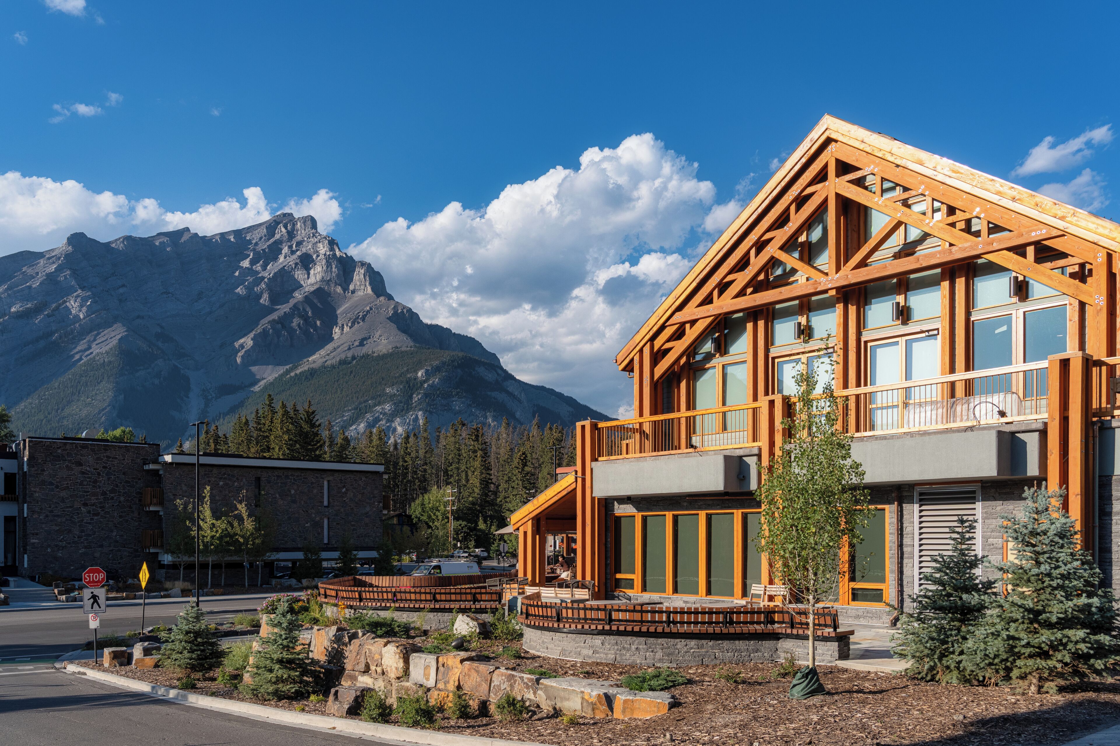 A modern building with large windows and a wooden facade, set against a mountain backdrop.
