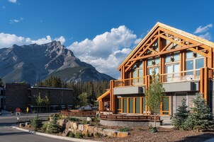Un edificio moderno con grandes ventanales y fachada de madera, con montañas al fondo.