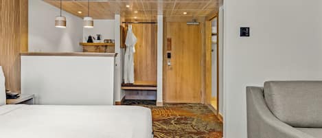 Una habitación de hotel con una cama, un sillón gris, techo de madera y alfombra estampada.