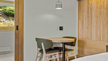 Habitación de hotel moderna con pared decorativa de madera, una pequeña mesa redonda con dos sillas, una cama y una ventana con vistas a zonas verdes.