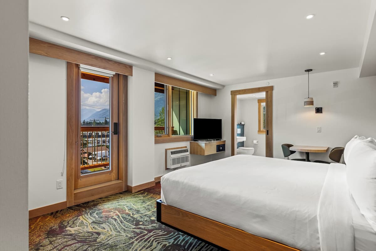 A hotel room with a large bed, a television, a desk with a chair, and a view of mountains through a window.