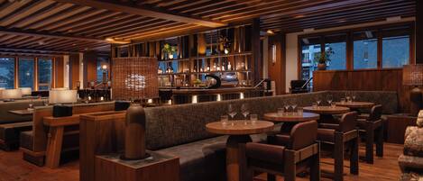 A modern restaurant with wooden flooring, cushioned seating, and a bar area.