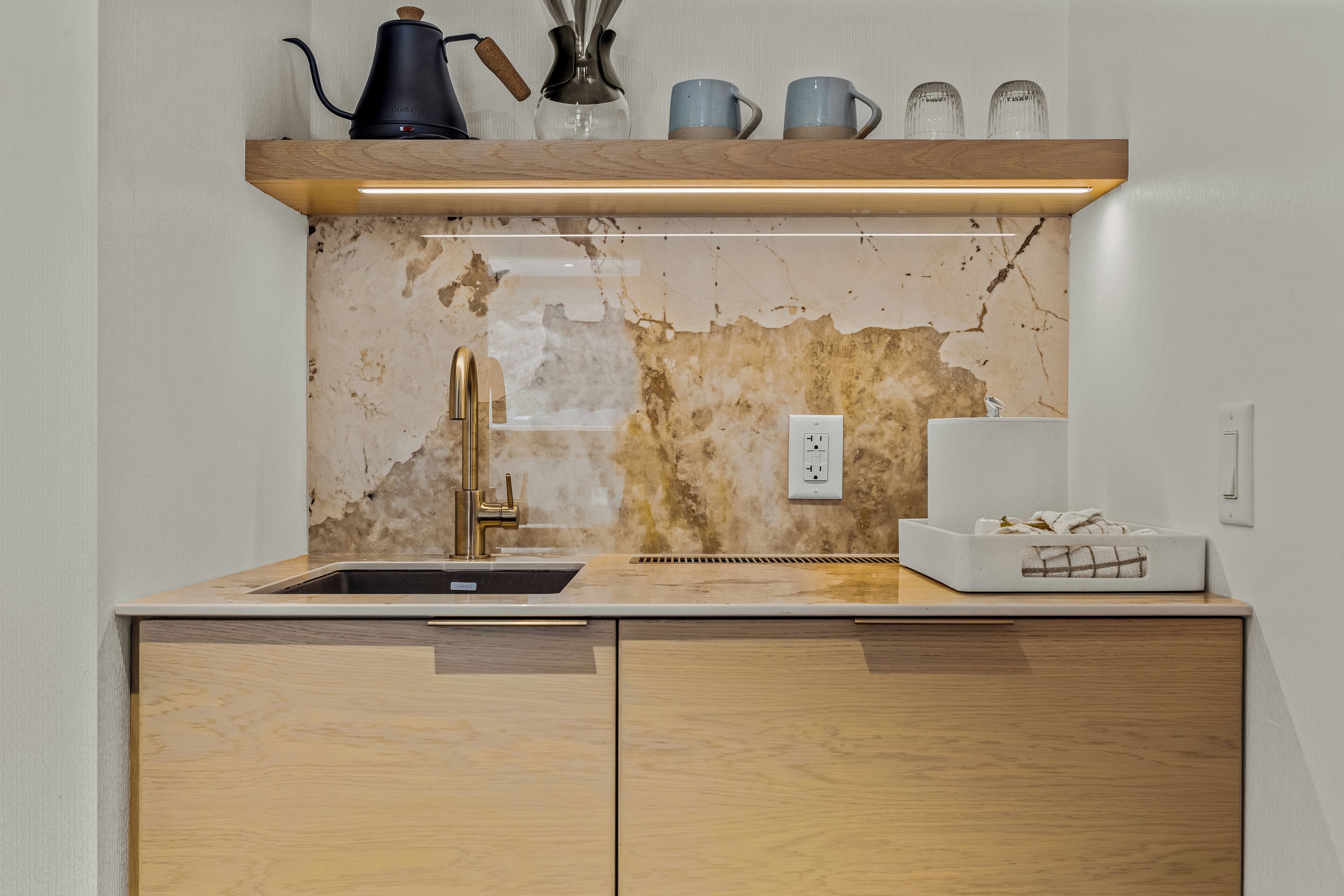 A kitchen with a marble backsplash, wooden cabinets, a sink, and a coffee maker on the countertop.