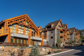A modern multi-story building with a distinctive wooden framework and stone facade, featuring balconies and large windows. - Otter Hotel (Banff)