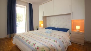 A bedroom with a large bed, two bedside lamps, a wardrobe, and a view through a window with curtains. - Charming flat just 350 metres from the beach with private balcony and sea view (Porec)