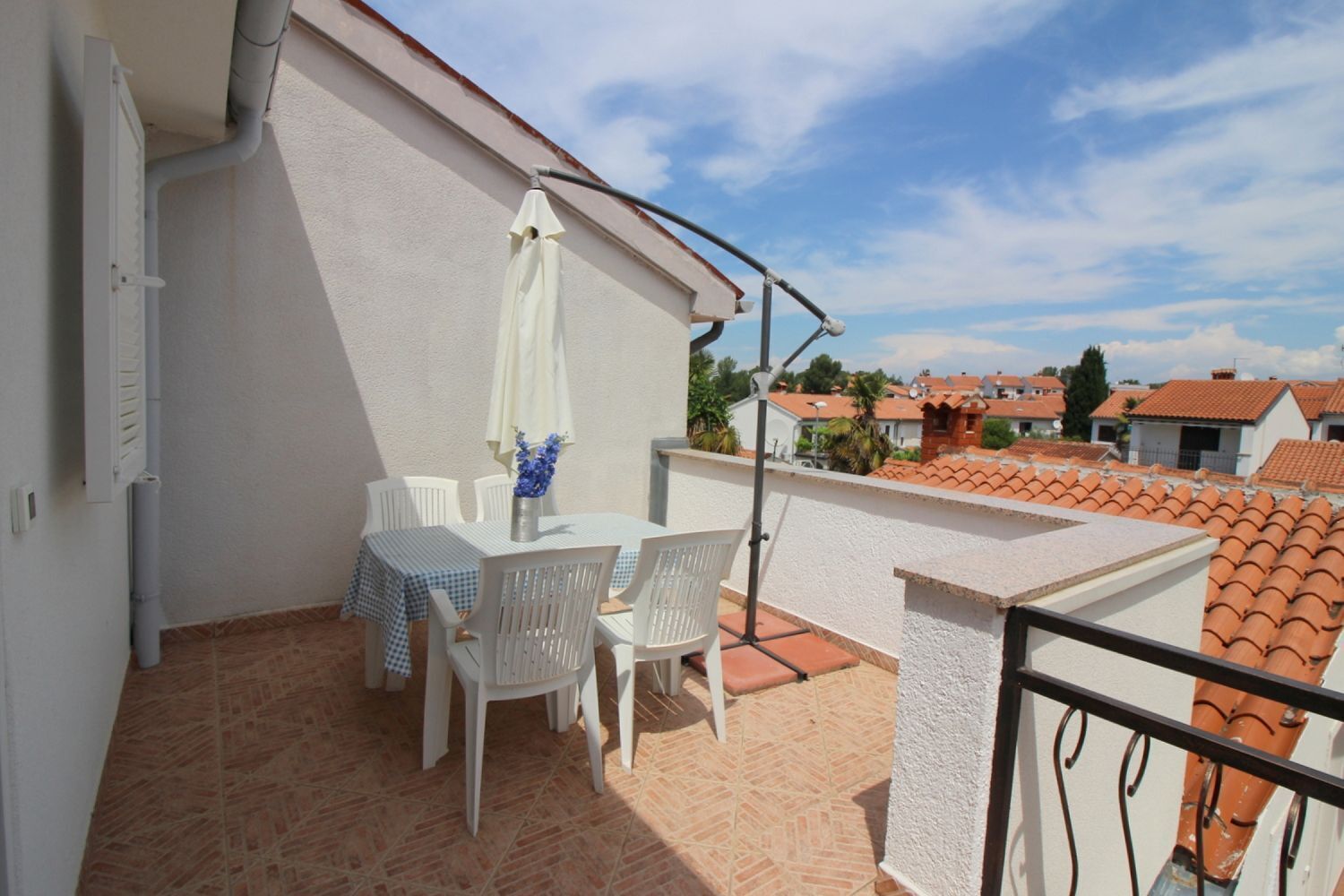 A balcony with a table and chairs, a white umbrella, and a view of neighboring houses.