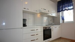 A modern kitchen with white cabinets, a built-in oven, and a window with a blue curtain. - Charming flat just 350 metres from the beach with private balcony and sea view (Porec)
