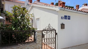 A white building with a tiled roof, a metal gate, and a stone wall. - Charming flat just 350 metres from the beach with private balcony and sea view (Porec)