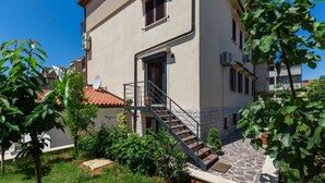 A two-story building with a stone-paved entrance, a satellite dish, and a staircase leading to the entrance. - Idyllic flat just a few minutes' walk from the beach with private balcony, air conditioning, barbecue, WiFi (Porec)