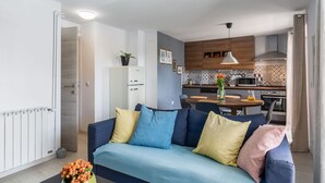A modern living room with a sofa, a dining table, and a kitchen in the background. - Modern flat with stylish furnishings, sea view, private balcony, barbecue, air conditioning, WiFi (Porec)