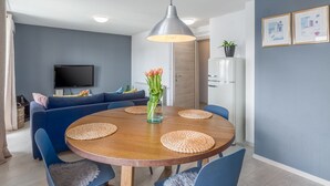 A modern living room with a round wooden dining table, blue chairs, a blue sofa, a flat-screen TV, and a ceiling light. - Modern flat with stylish furnishings, sea view, private balcony, barbecue, air conditioning, WiFi (Porec)