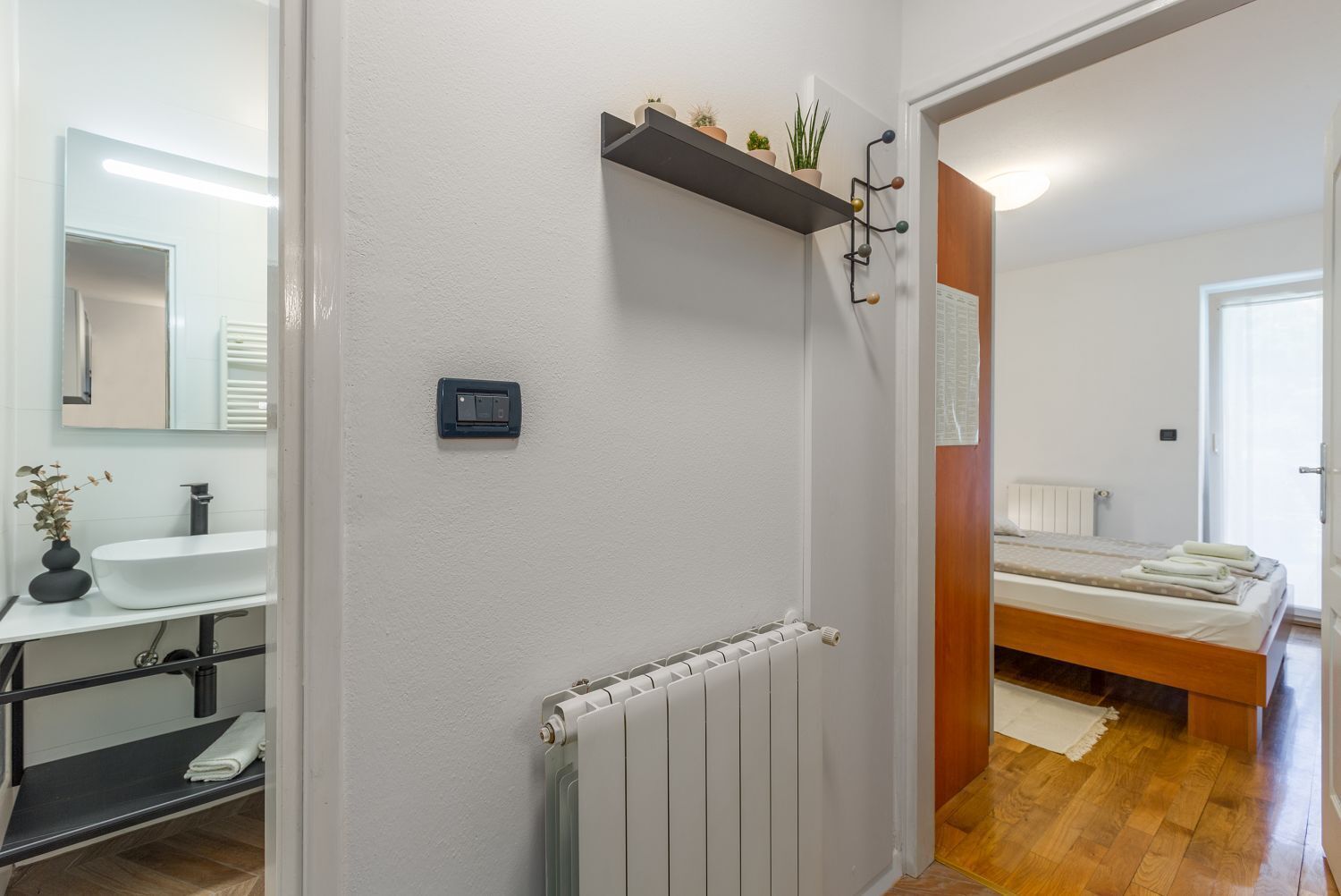 Ein modernes Badezimmer mit einem weißen Waschbecken, einem Spiegel, einem Handtuchhalter und einer Heizung.