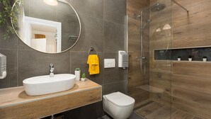 A modern bathroom with a round mirror, a white sink, a toilet, and a glass-enclosed shower area.