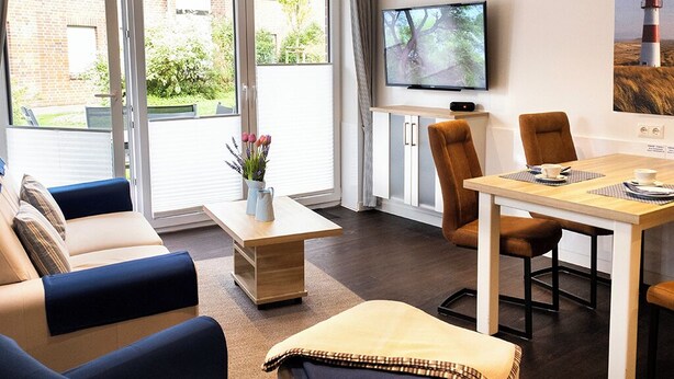 Ein modernes Wohnzimmer mit einer Couch, einem Couchtisch, einem Esstisch mit Stühlen, einem Fernseher und einem Gemälde eines Leuchtturms.