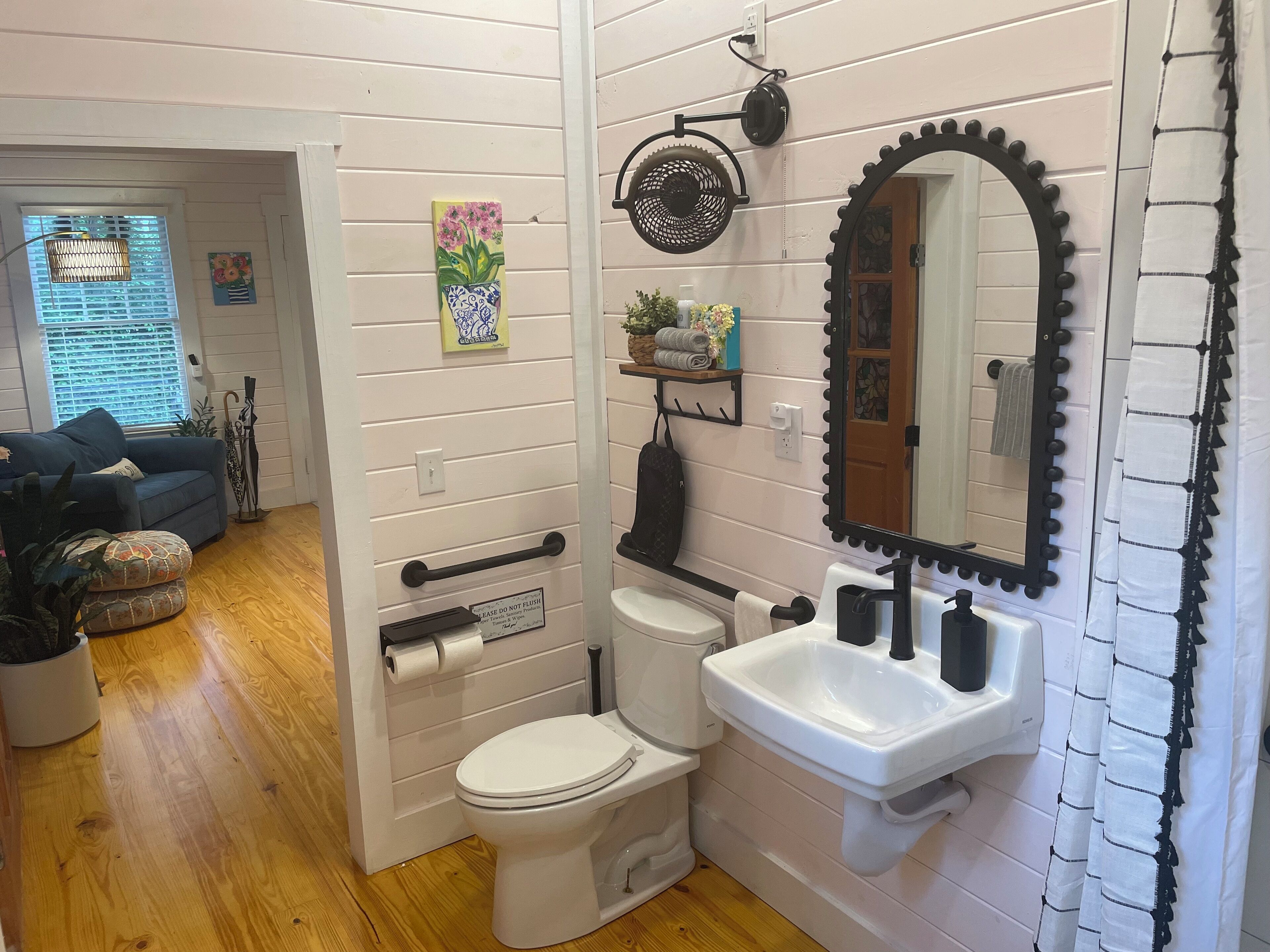 A bathroom with a toilet, sink, and mirror. There is a shelf with towels and a small plant.