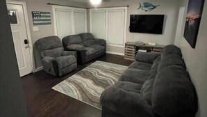 Una sala de estar con un sofá gris, un sillón reclinable gris y una alfombra estampada.