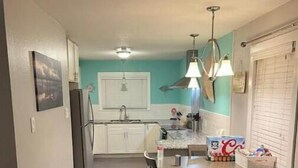 Una cocina estrecha con comedor, refrigerador, pileta y ventana con persianas.