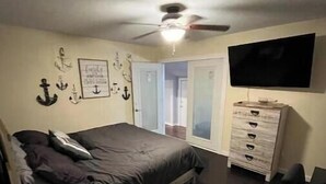 Un dormitorio con cama, cómoda, televisor y ventilador de techo.