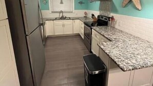 Cocina compacta con armarios blancos, refrigerador de acero inoxidable, encimera de granito y una decoración con forma de estrella de mar en la pared.