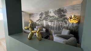 A modern living room with a large painting of a forest, a golden sculpture, grey sofas, and a unique floor lamp. - Historic center, lovely air-conditioned apartment with terrace.  (AIX EN PROVENCE)