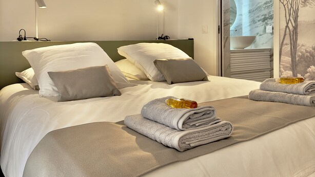 A neatly made bed with pillows, a folded towel, and a bottle of lotion on it. - Historic center, lovely air-conditioned apartment with terrace.  (AIX EN PROVENCE)
