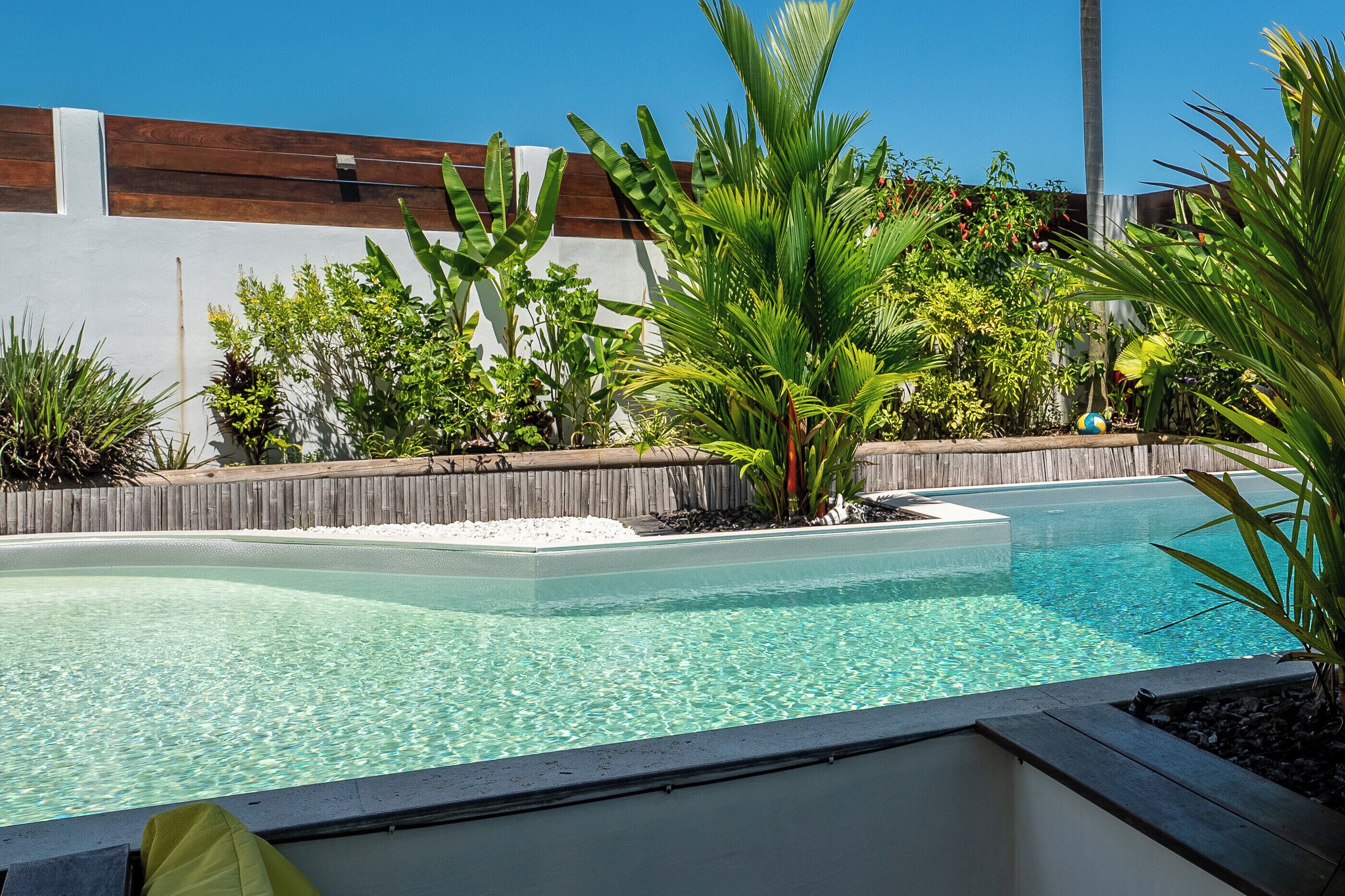 Una piscina cristalina rodeada de plantas tropicales y una valla de madera.