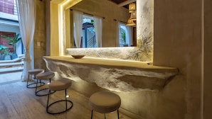 A bar area with a rustic stone counter, three stools, and a large mirror reflecting the interior. - Casa Fernández Cartagena (Cartagena)