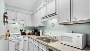 A kitchen with white cabinets, a stove, a microwave, and a sink. - Okaloosa Island Castaway-Pets Allowed (Fort Walton Beach)