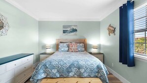 A bedroom with a bed, bedside tables, a bench, a wall-mounted turtle decoration, and a window with blinds. - Okaloosa Island Castaway-Pets Allowed (Fort Walton Beach)