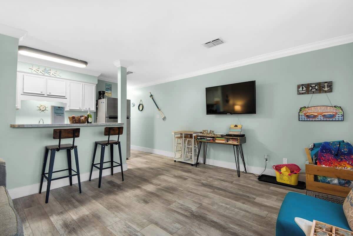 A modern kitchen with bar stools, a dining table, and a flat-screen TV mounted on the wall.