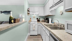 A compact kitchen with white cabinets, a built-in oven, a microwave, and a sink. - Okaloosa Island Castaway-Pets Allowed (Fort Walton Beach)