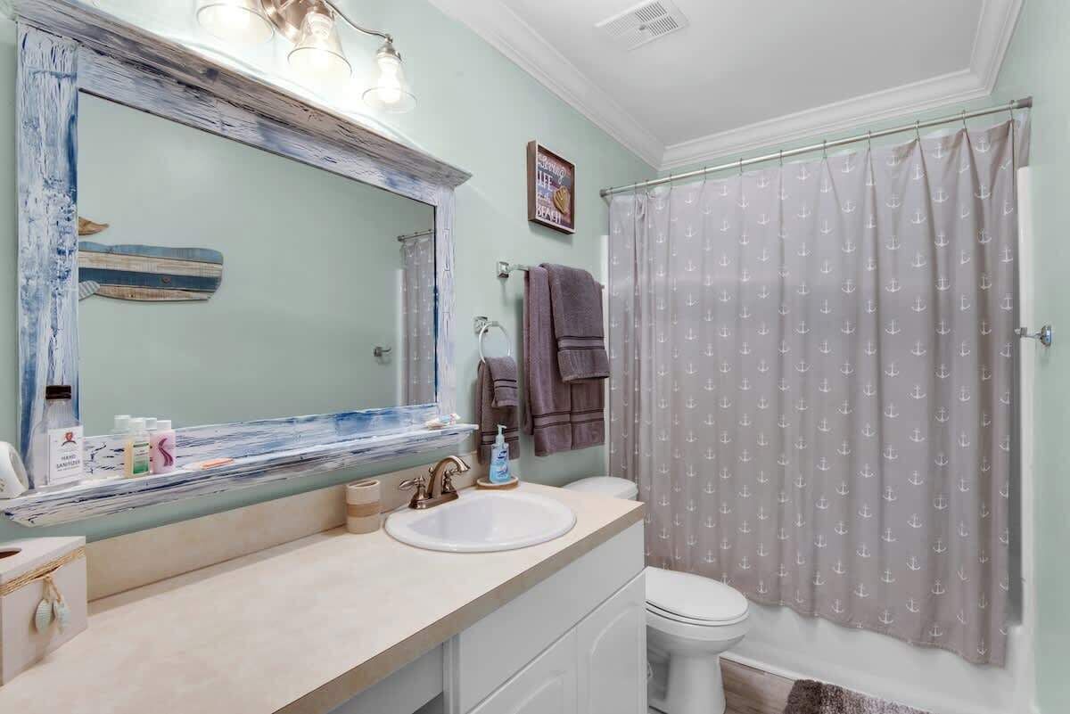 Een badkamer met een grote spiegel, een wastafel en een toilet. Er is een douchegordijn met een patroon, en handdoeken hangen aan de muur.