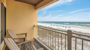 Un balcón con dos sillas Adirondack, vista a la playa y cielo despejado.