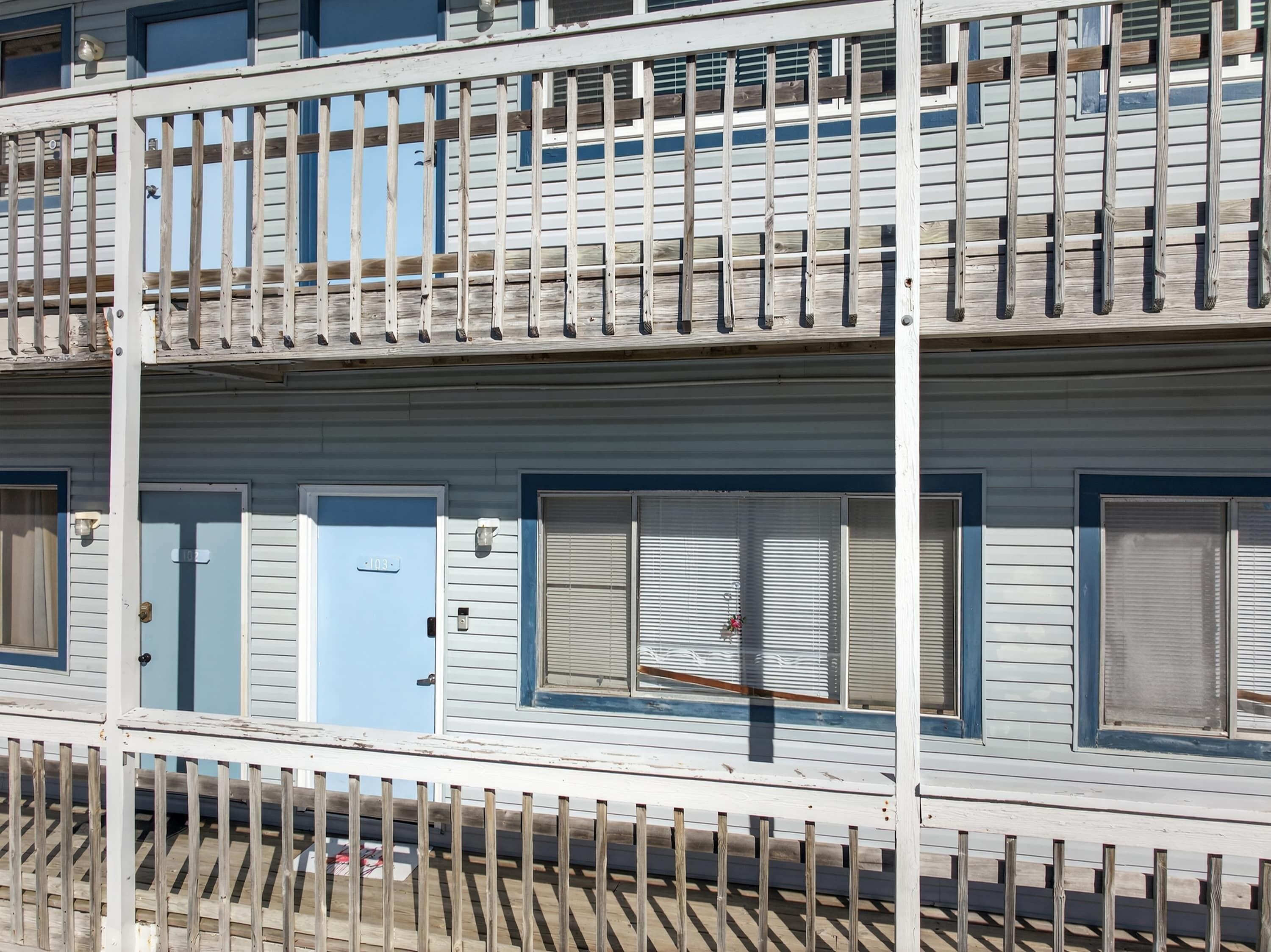 A multi-story building with a balcony, a blue door, and a window with blinds.