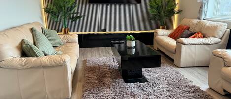 Een moderne woonkamer met een zithoek, een salontafel en een aan een wand met verticale lijnen bevestigde televisie.