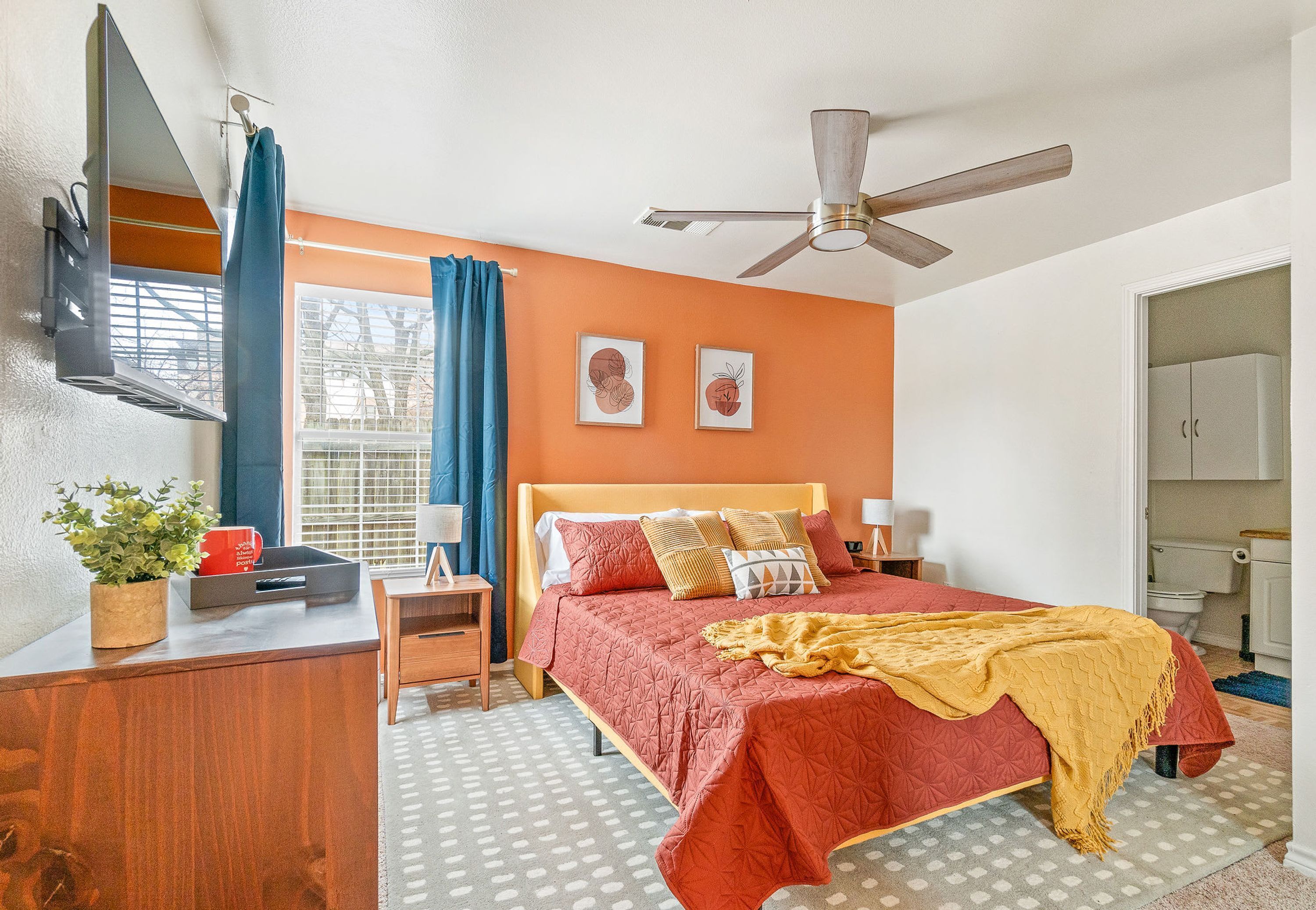 Un dormitorio con cama, escritorio, ventilador de techo y ventana con cortinas.