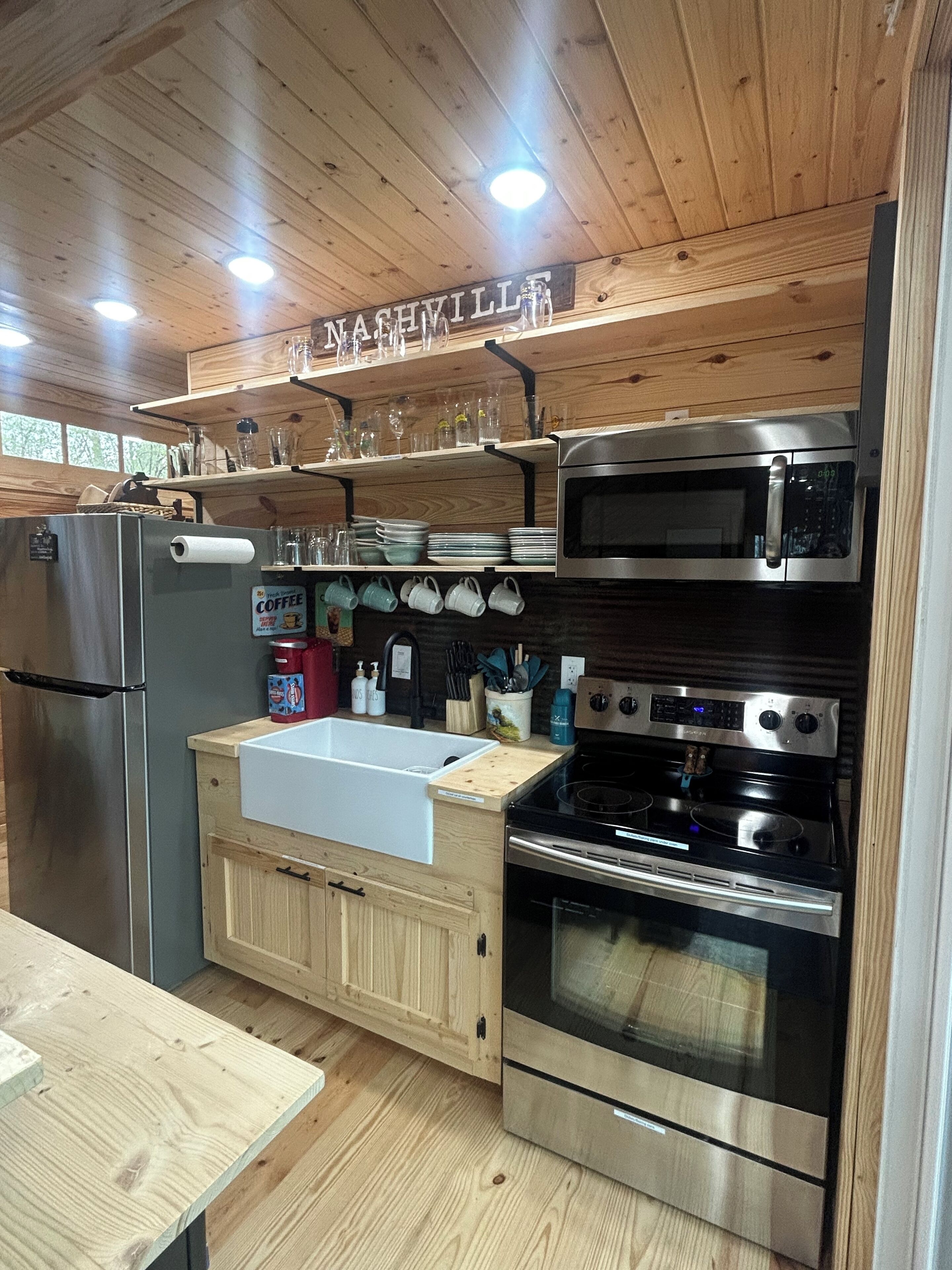Una cocina con armarios de madera, electrodomésticos de acero inoxidable, un lavamanos y una encimera con cristalería y utensilios.