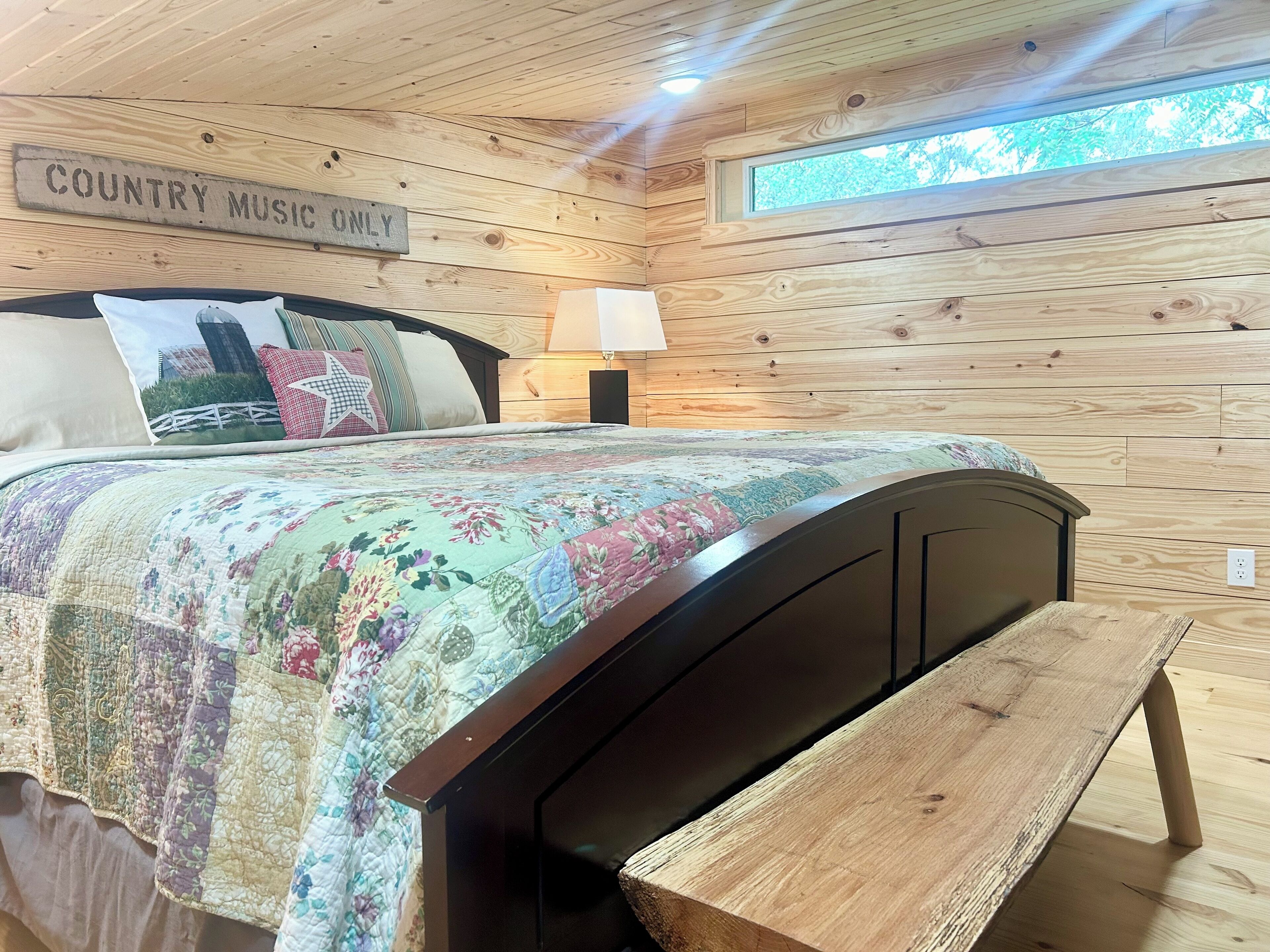 A wooden-paneled room with a bed, a bench, a nightstand, and a sign that reads "COUNTRY MUSIC ONLY".