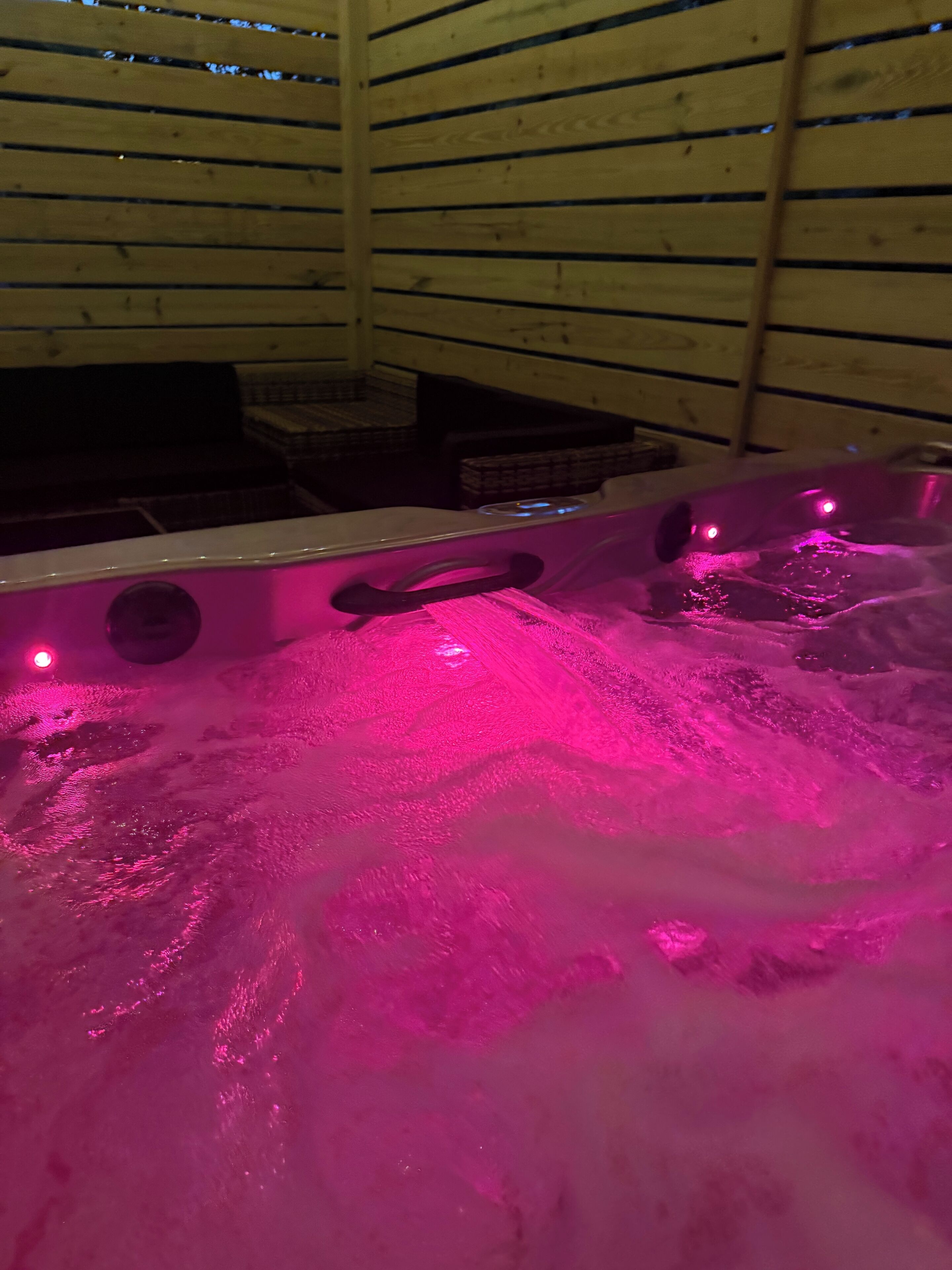 Un jacuzzi con iluminación rosa dentro de una estructura de madera.